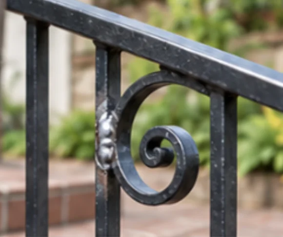Decorative steel staircase railing with a repaired weld on a scroll flourish